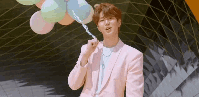 a man in a pink suit is holding a bunch of balloons in his hand .