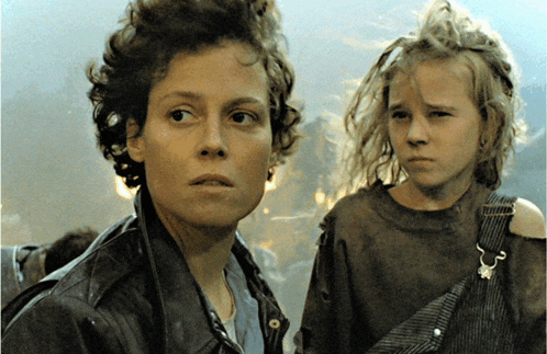 a woman in a leather jacket and overalls stands next to a young girl