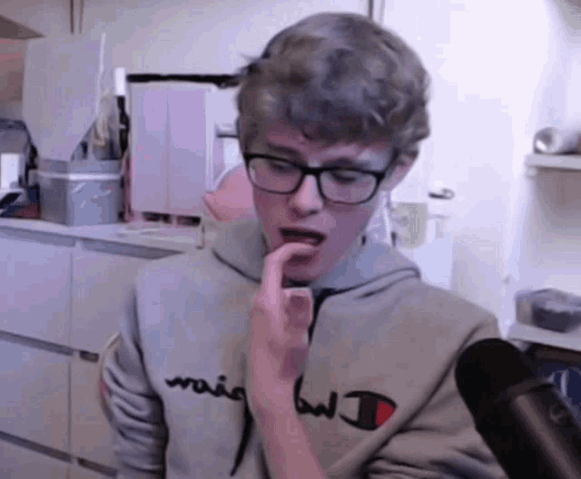 a young man wearing glasses and a champion sweatshirt bites his thumb