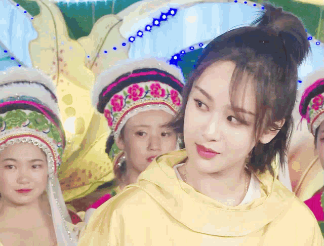 a woman in a yellow hoodie stands in front of a group of women wearing traditional hats