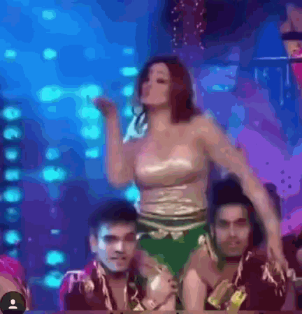a woman is dancing on a stage with a group of people behind her .