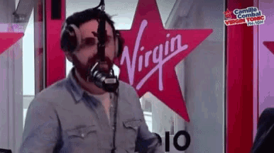 a man is standing in front of a microphone in front of a virgin logo .
