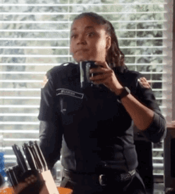 a woman in a police uniform is drinking from a cup