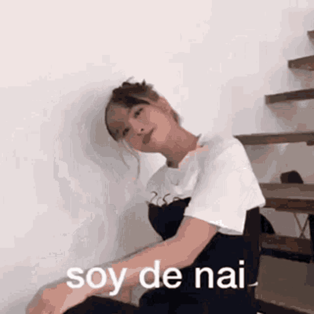 a woman is sitting on a staircase with the words soy de nai written on the wall .
