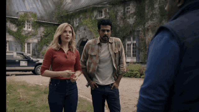 a woman in a red shirt stands next to a man in a plaid shirt and a man in a blue vest