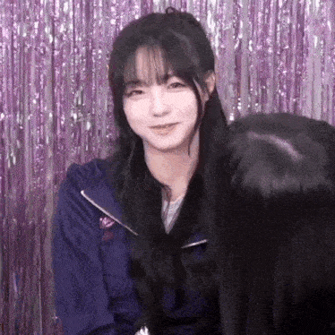 a girl with long black hair and bangs is standing in front of a purple curtain .