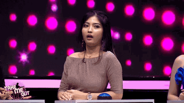 a woman is sitting in front of a screen that says take me out