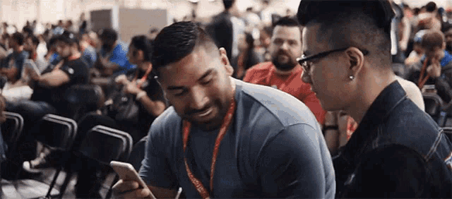 a man with a lanyard around his neck looks at another man 's phone