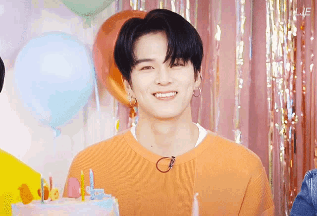 a young man is smiling in front of a cake with candles and balloons