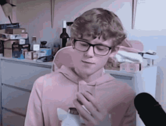 a boy wearing glasses and a pink hoodie is holding a bottle