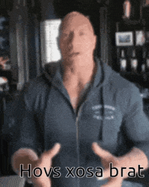 a man in a blue hoodie is standing in a room with his hands outstretched and says hovs xosa brat .