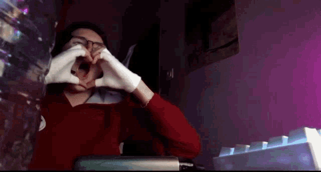 a man wearing glasses and white gloves is making a heart with his hands .
