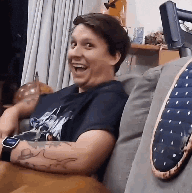 a man with a tattoo on his arm is sitting on a couch with a watch on his wrist
