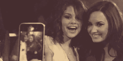 two women are taking a selfie with a cell phone and smiling .