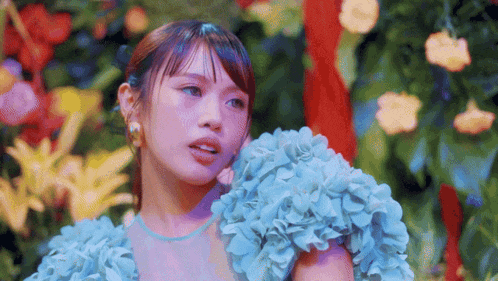 a woman in a blue dress is standing in front of a bunch of flowers .