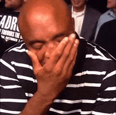 a bald man wearing a striped shirt is covering his face with his hands .
