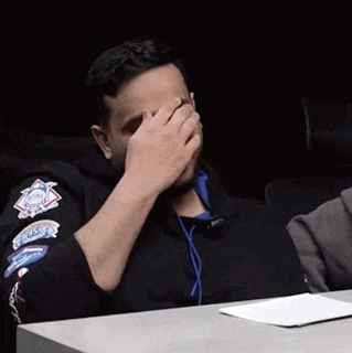 a man is covering his face with his hand while wearing a black jacket with patches on it