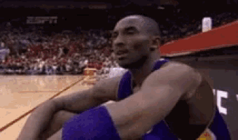 a basketball player is sitting on the court with his hands on his knees .