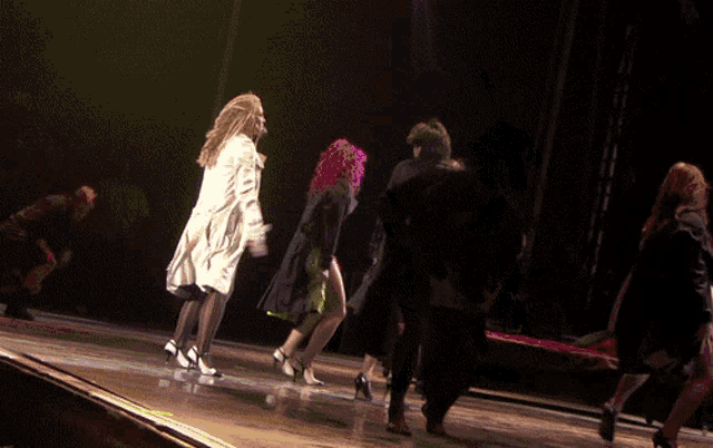 a group of people are dancing on a stage and one of them has pink hair