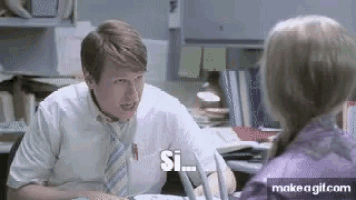 a man and a woman are sitting at a desk talking to each other .