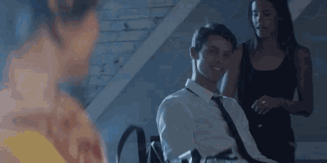 a man in a white shirt and tie is sitting in a chair with a woman standing behind him .