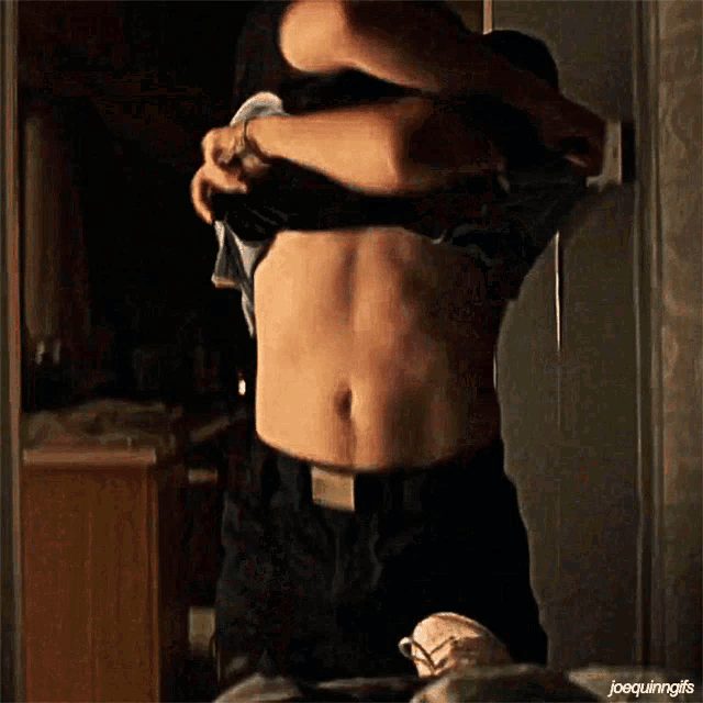 a man is taking off his shirt in a dark room with joequingifs written on the bottom