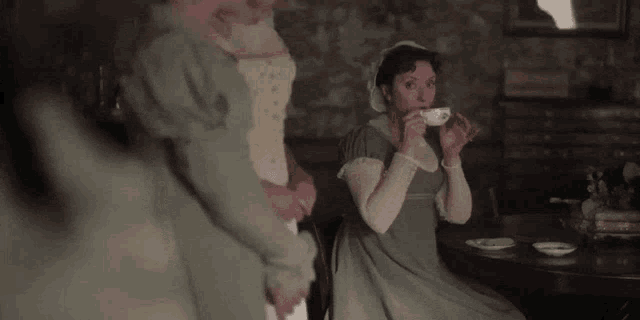 a woman in a green dress is drinking tea from a cup while sitting at a table .