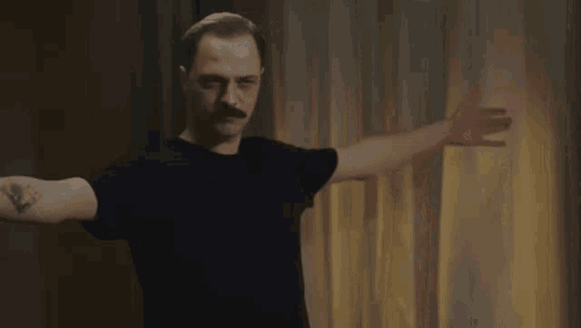 a man with a mustache is standing with his arms outstretched in a room .