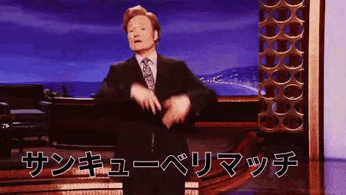 a man in a suit and tie is dancing on a stage in front of a sign that says " サンキュー ベリマッチ "