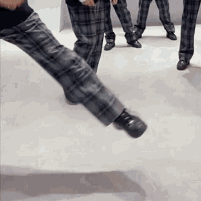 a person wearing plaid pants and black shoes is standing on a white floor .