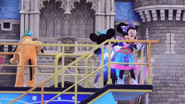 mickey mouse and pluto are dancing on a platform in front of a castle