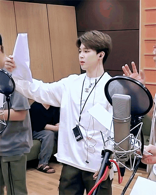 a man in a white shirt stands in front of a microphone holding a piece of paper