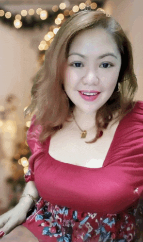 a woman in a red top smiles in front of a blurry background
