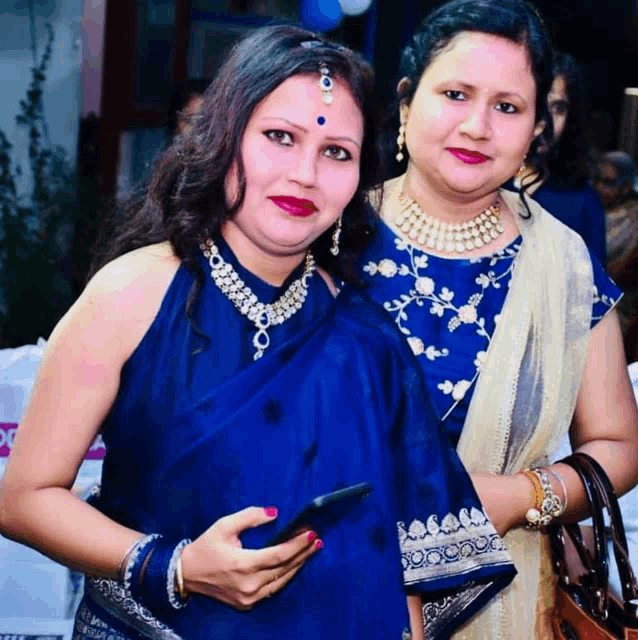 two women are posing for a picture and one is holding a cellphone