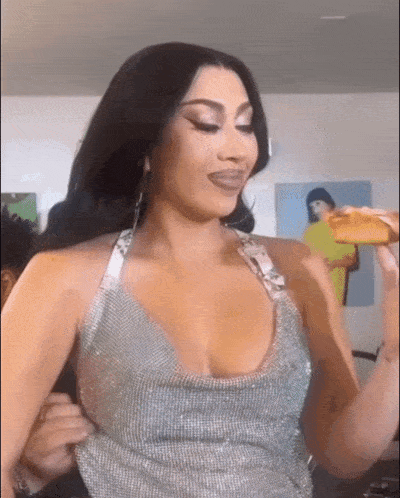 a woman in a silver dress is holding a slice of pizza in her hand