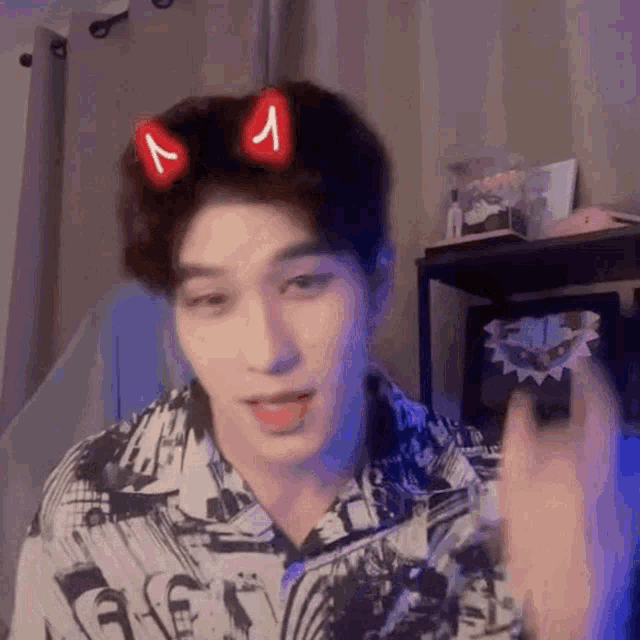 a young man wearing a shirt with devil horns on his head is making a funny face .