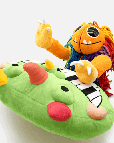 a stuffed monster is sitting on top of a green monster pillow