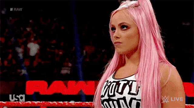 a female wrestler with pink hair is standing in a ring .