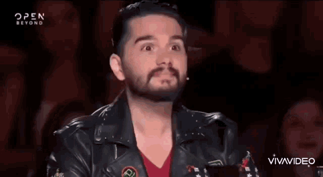 a man with a beard is wearing a leather jacket and making a funny face .