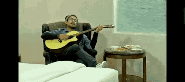 a man is sitting in a chair playing an acoustic guitar