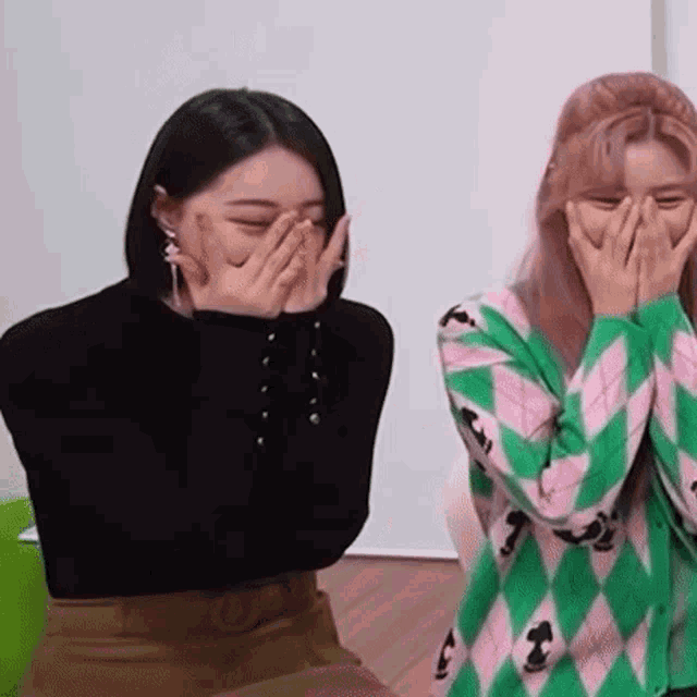 two girls are covering their faces with their hands while sitting next to each other .