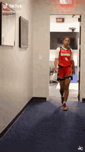 a woman in a red jersey with the number 4 on it walks down a hallway