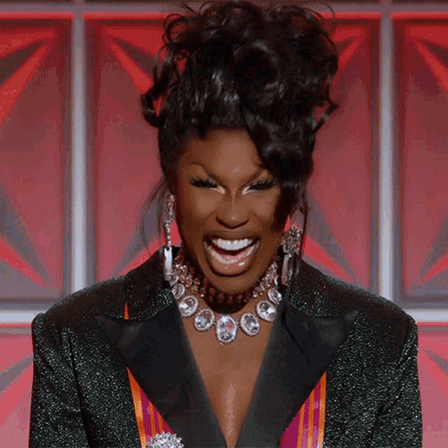 a woman wearing a tuxedo and a necklace smiles with her mouth open