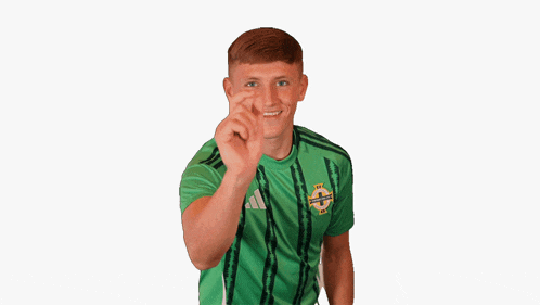a young man wearing a green adidas shirt is making a funny face