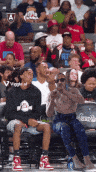 a shirtless man sits in the stands at a basketball game sponsored by wiggle.al