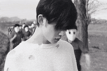 a black and white photo of a man wearing a white sweater and a mask .