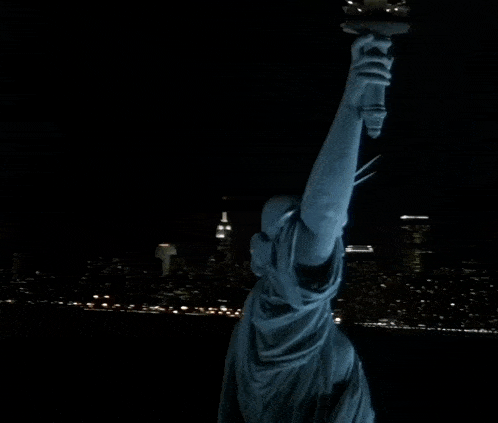the statue of liberty is lit up at night with a city skyline in the background