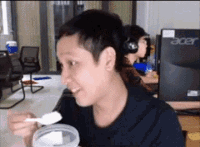 a man wearing headphones is eating ice cream with a spoon in front of an acer computer monitor
