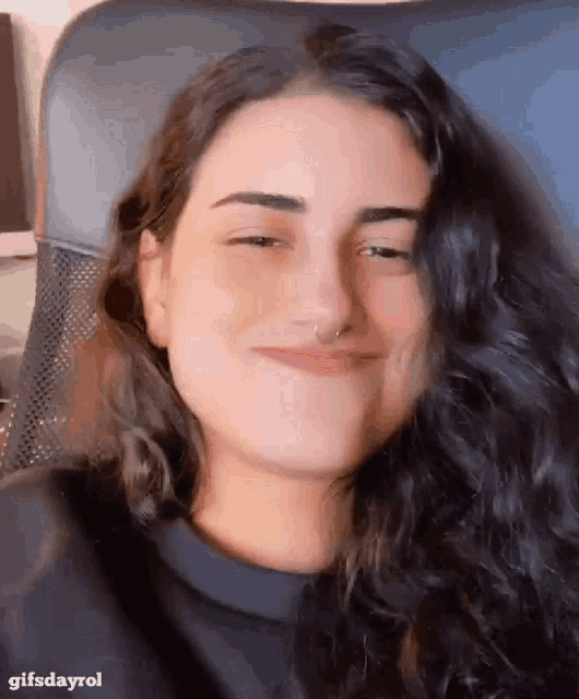 a woman with a nose ring is sitting in a chair and smiling .