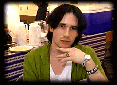 a man wearing a watch and a ring on his finger looks at the camera